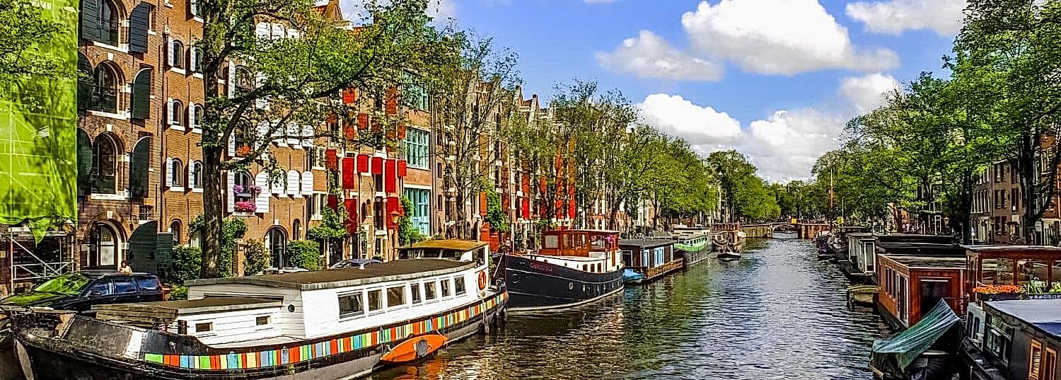 a quiet canal in amsterdam with house boats parked off to the side on a bright, sunny day