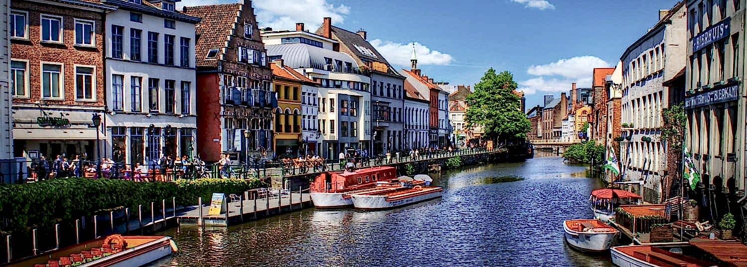 charming canal with a few boats anchored to the side surrounded by old world buildings in belgium