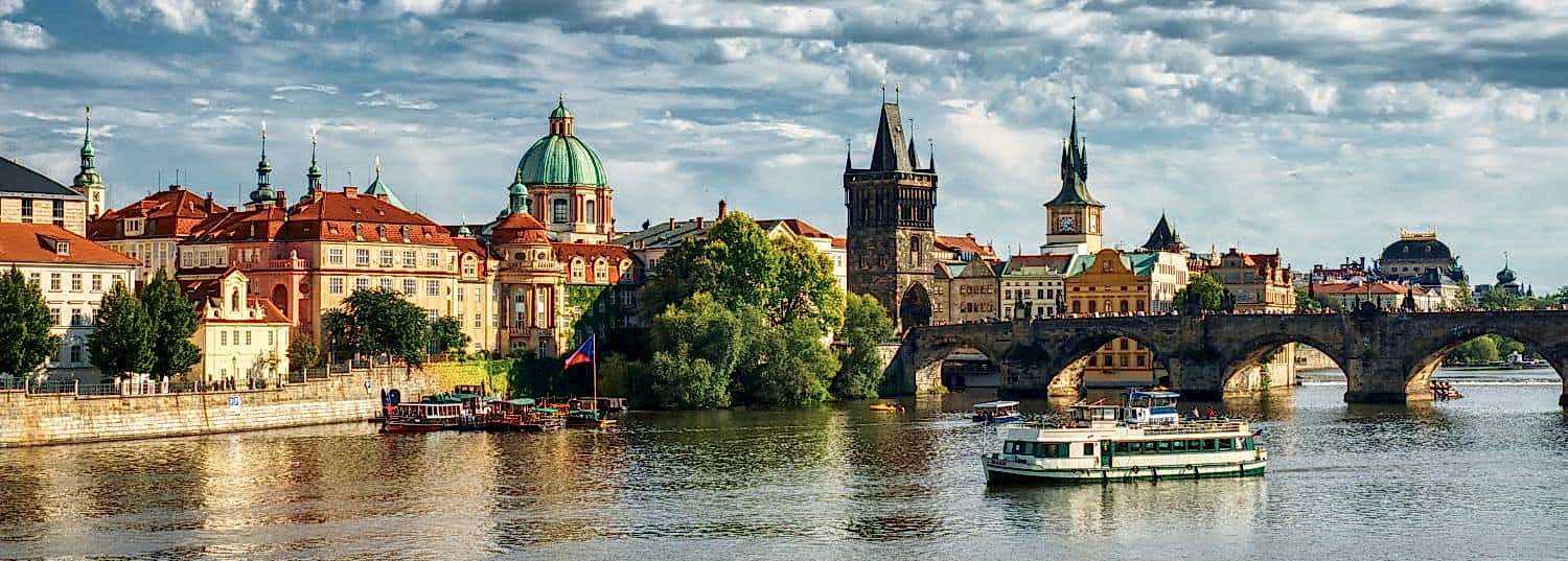the beautiful old town of prague viewed from the river with a single boat passing by