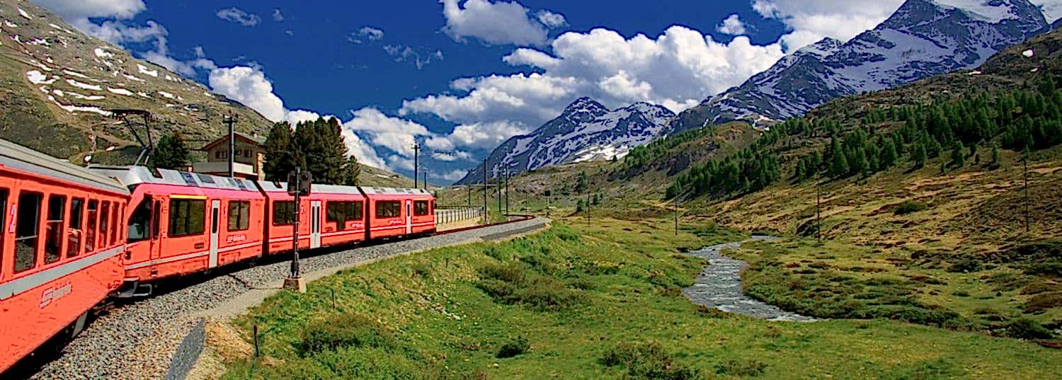 a red train car moving through the mountains of switzerland leaving behind green fields for snowcapped mountains