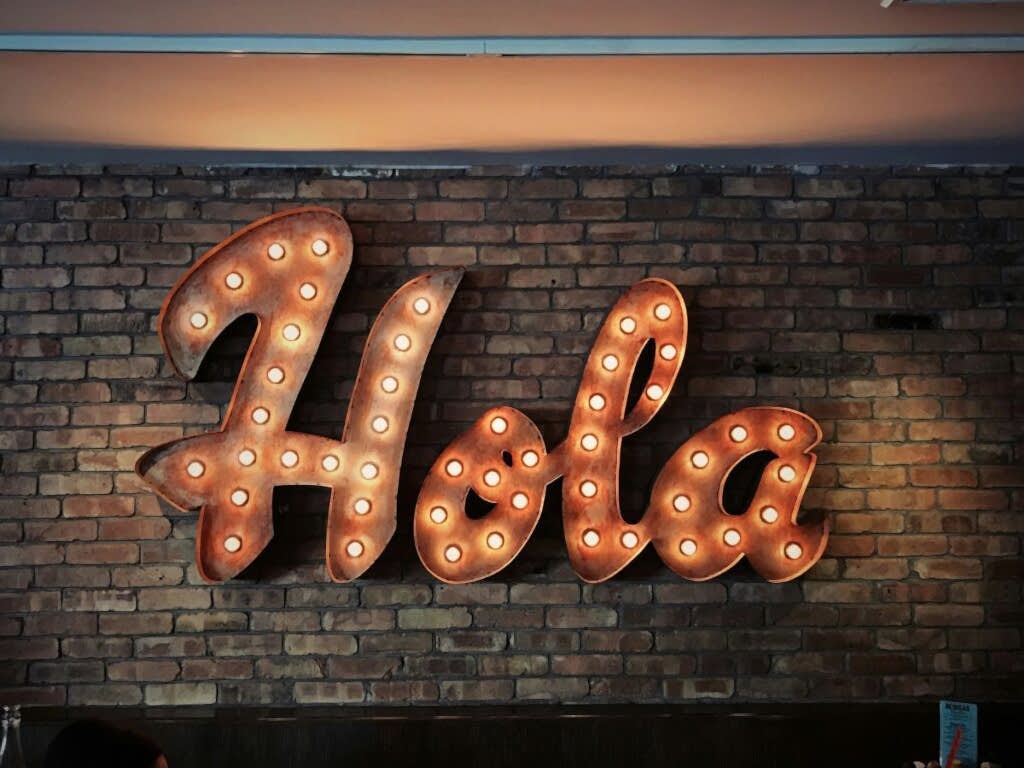 giant copper colored sign with lights that says hola on a brick wall