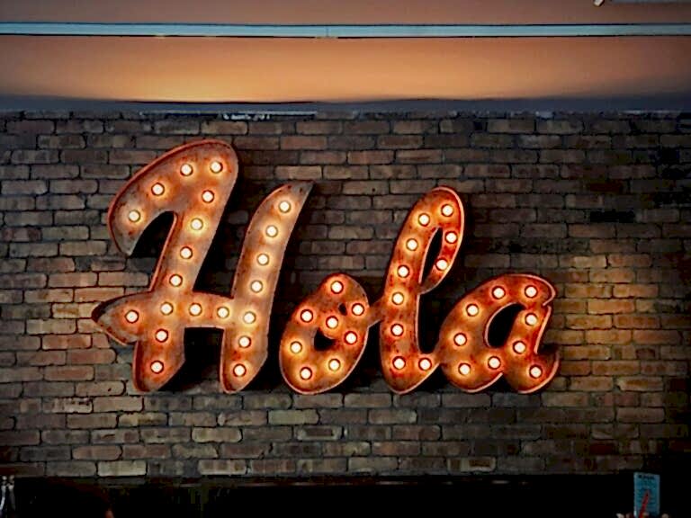 giant copper colored sign with lights that says hola on a brick wall