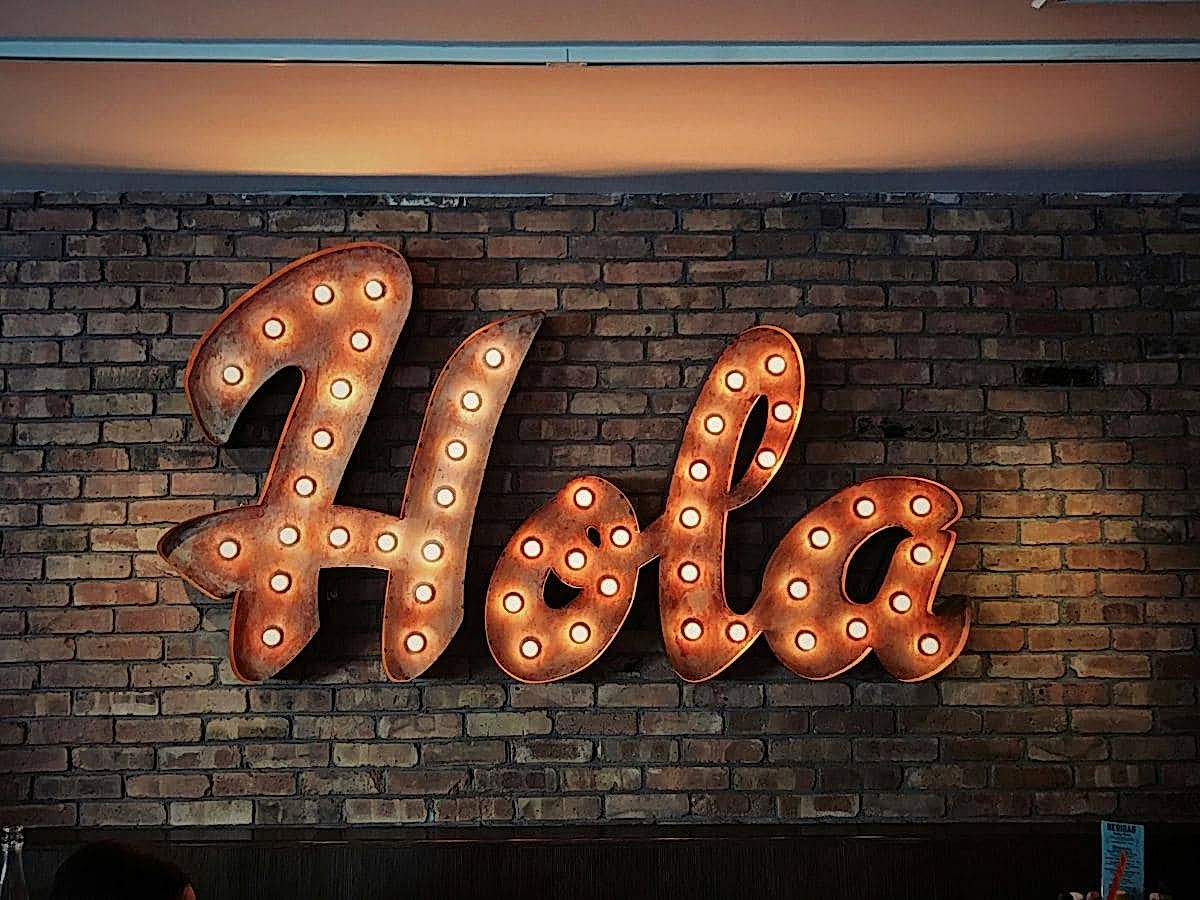 giant copper colored sign with lights that says hola on a brick wall