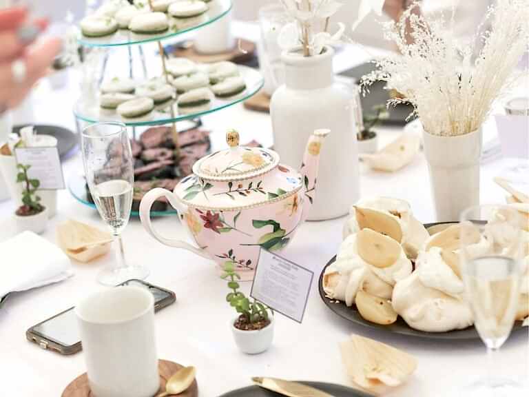 white table cloth covered table with small china tea cups and a tea pot surrounded by vegan afternoon tea sweets in london
