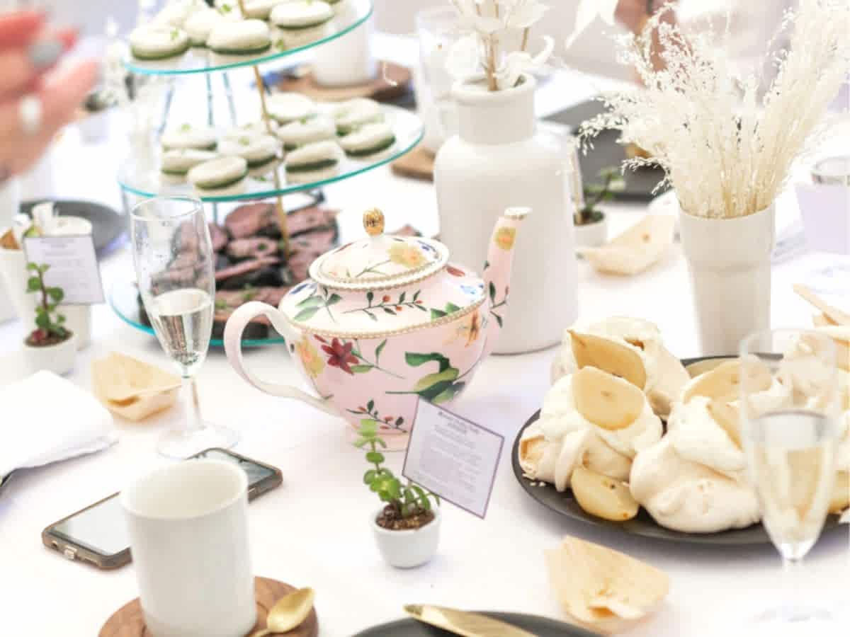 white table cloth covered table with small china tea cups and a tea pot surrounded by vegan afternoon tea sweets in london